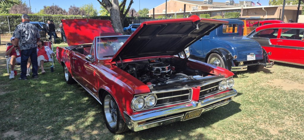 A red 1964 Pontiac GTO convertible with the hood up at the 2026 Valley Nationals